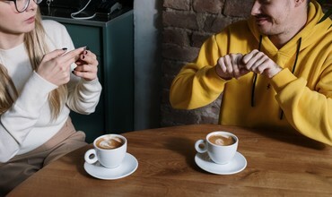 dwie osoby przy kawiarnianym stoliku; rozmawiają w języku migowym
